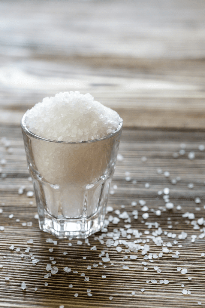 Is It Safe to Drink Salt Water? This is a photograph of sea salt in a glass cup on a wooden table.